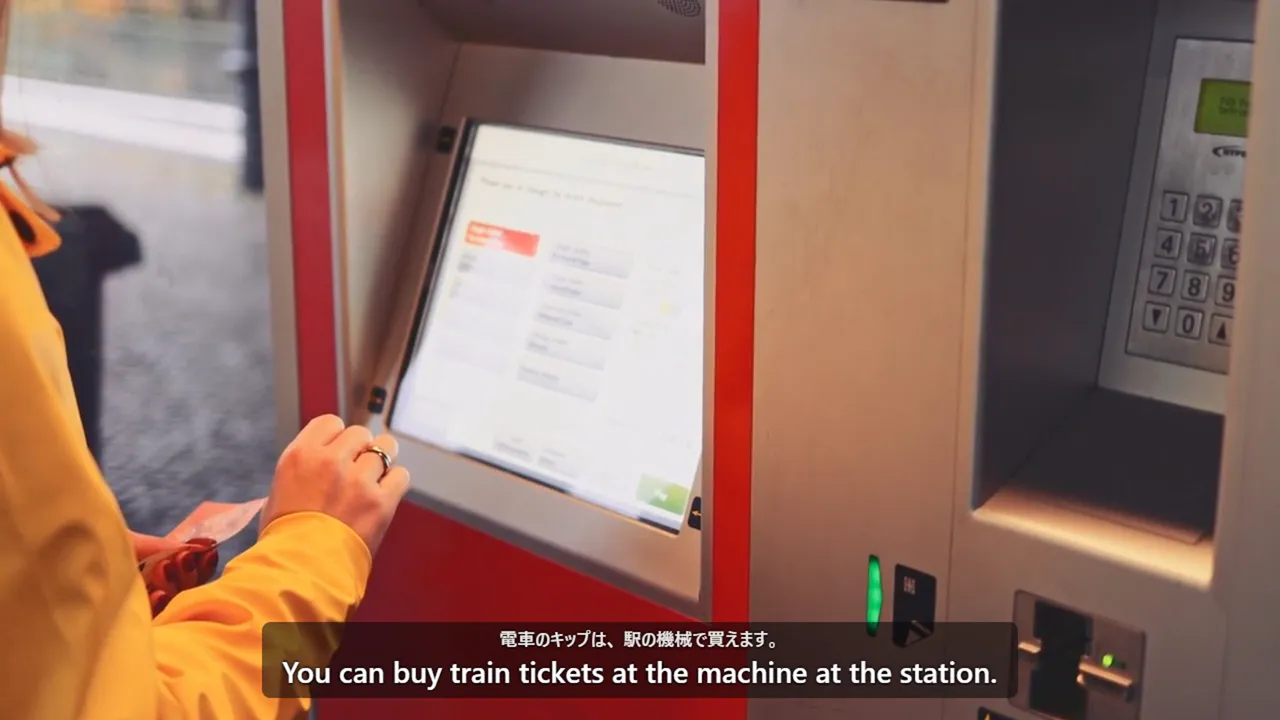 A hand at a ticket machine, with the Japanese line and its English subtitle over the video